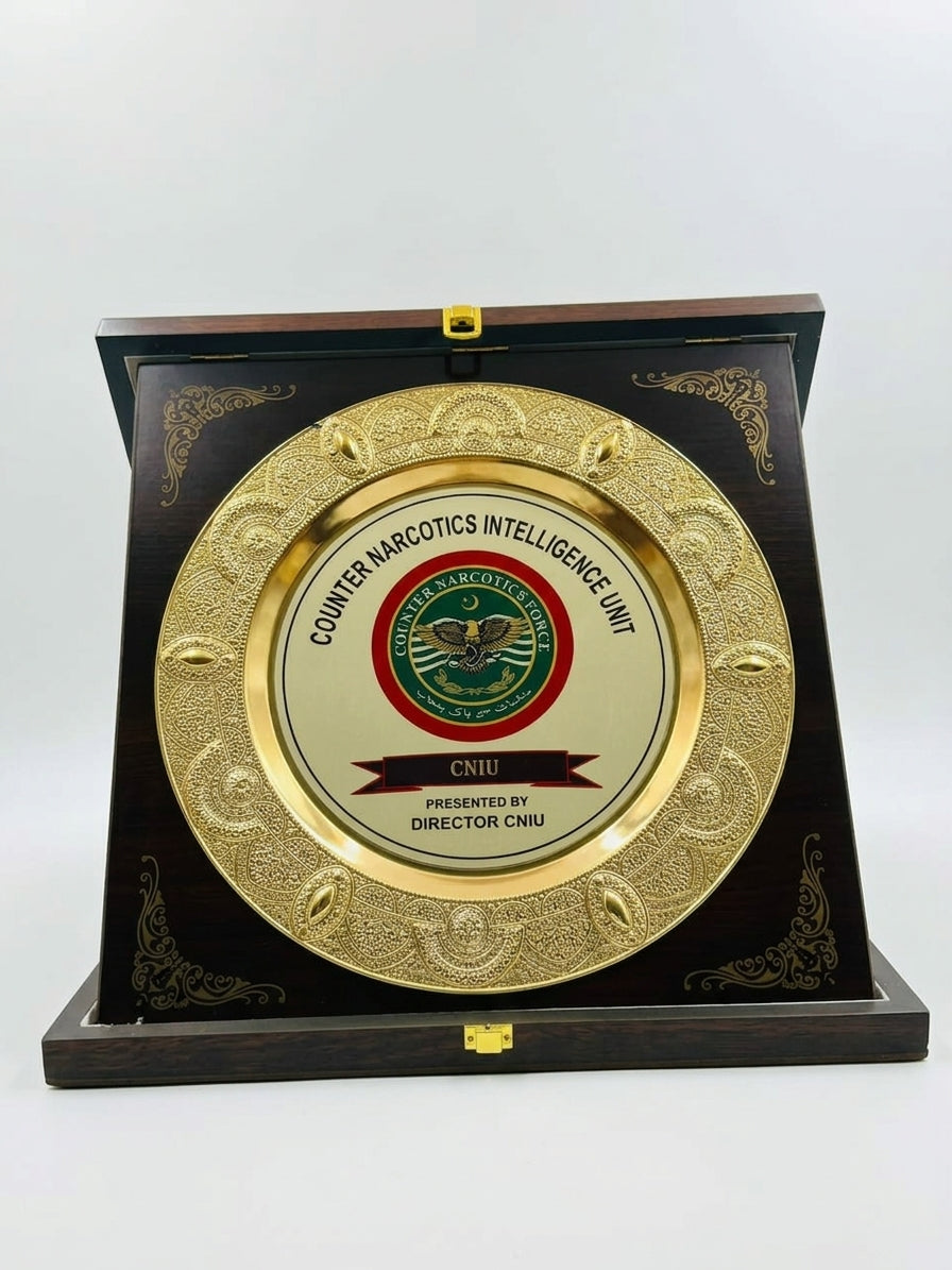 A round gold-toned metal plaque with the Counter Narcotics Intelligence Unit (CNIU) emblem, mounted on a dark wooden display stand against a plain white background.