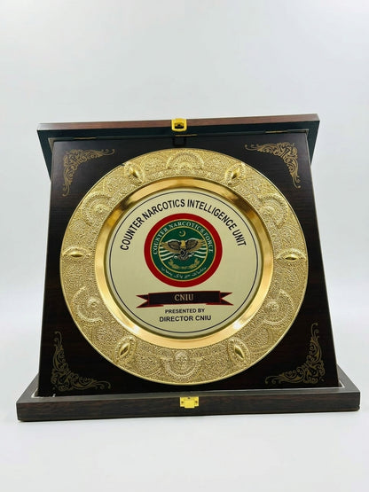 A round gold-toned metal plaque with the Counter Narcotics Intelligence Unit (CNIU) emblem, mounted on a dark wooden display stand against a plain white background.