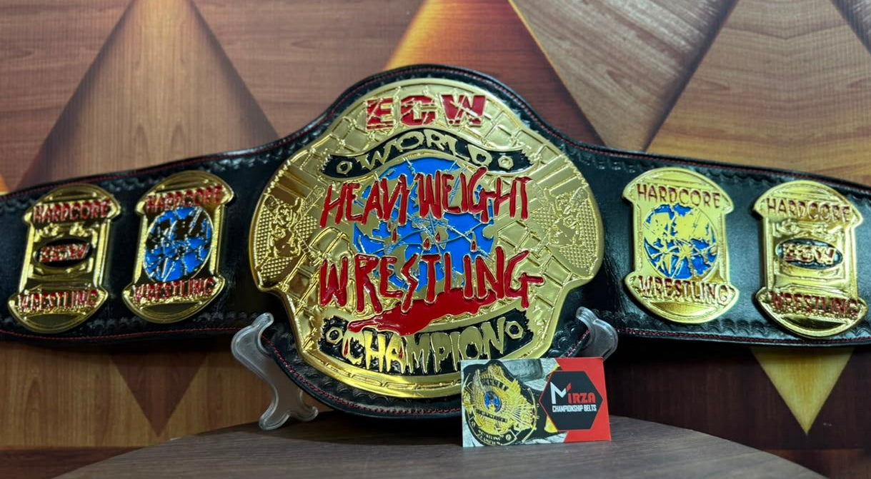 A black and gold 2024 COW World Heavy Wrestling Championship belt displayed on a small stand, with a small card in front, set against a geometric wood-patterned background.