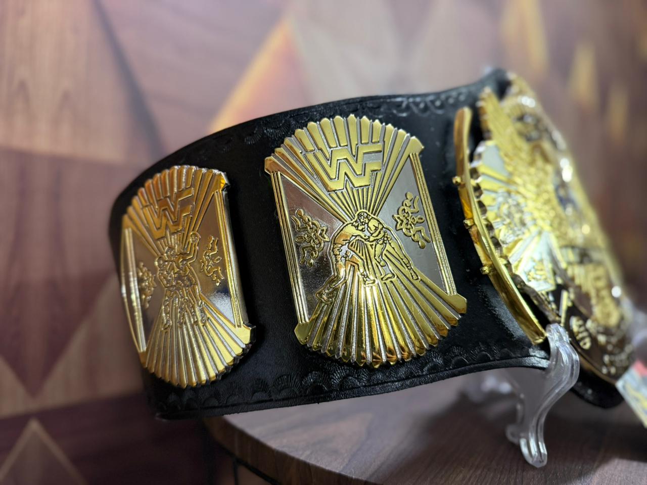 Black championship belt with gold and silver medallions on a wooden surface.